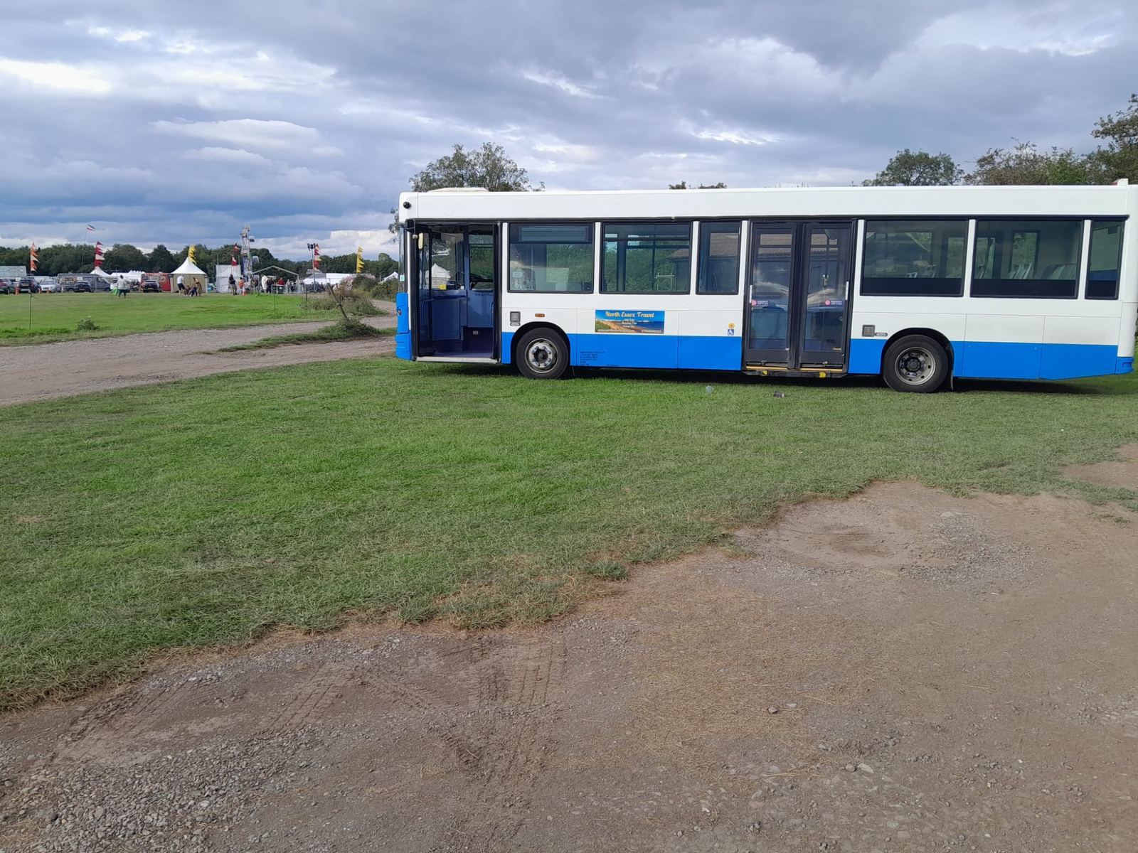 White bus with a blue stripe parked on grass beside a field under a cloudy sky