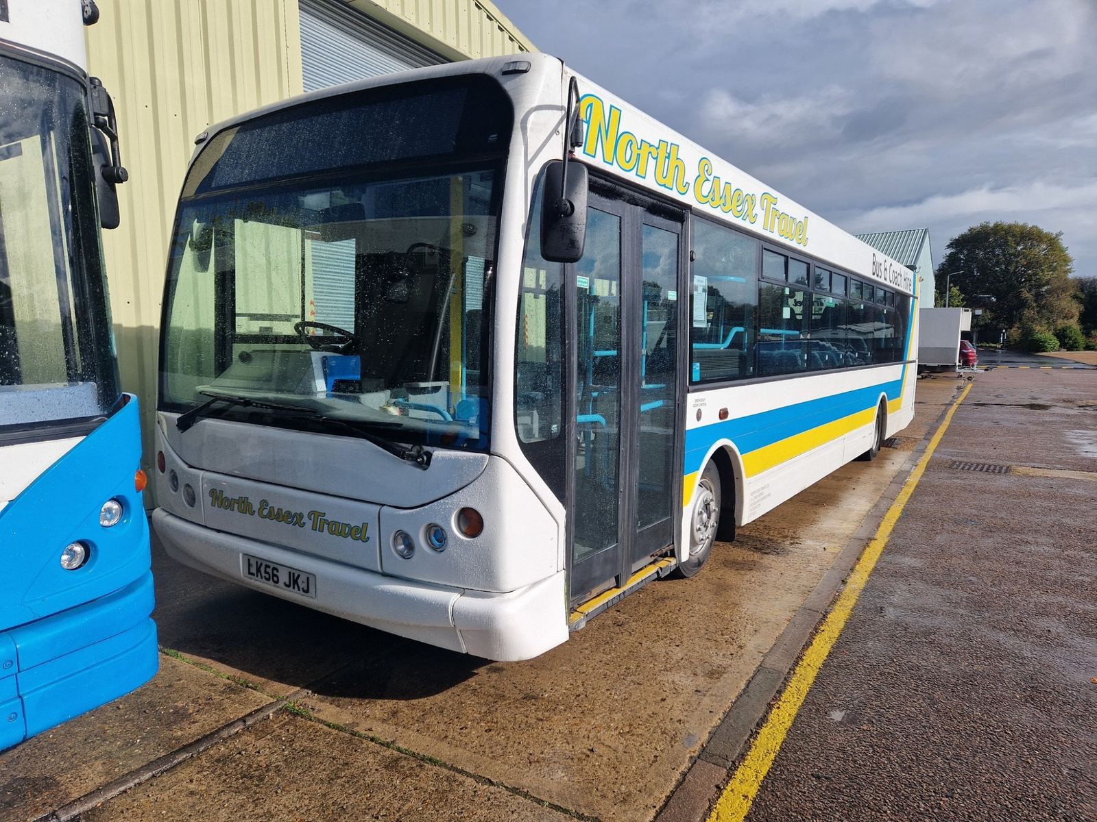 White bus with blue and yellow stripes and North Essex Travel lettering parked beside a depot building