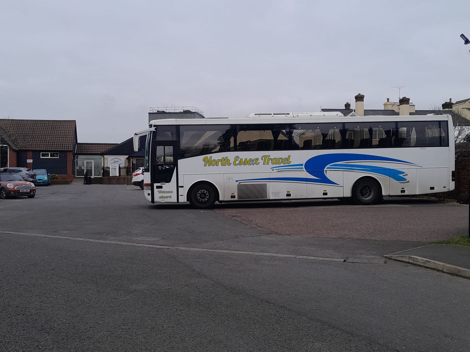 White North Essex Travel coach with a blue swoosh parked in front of houses and a car park