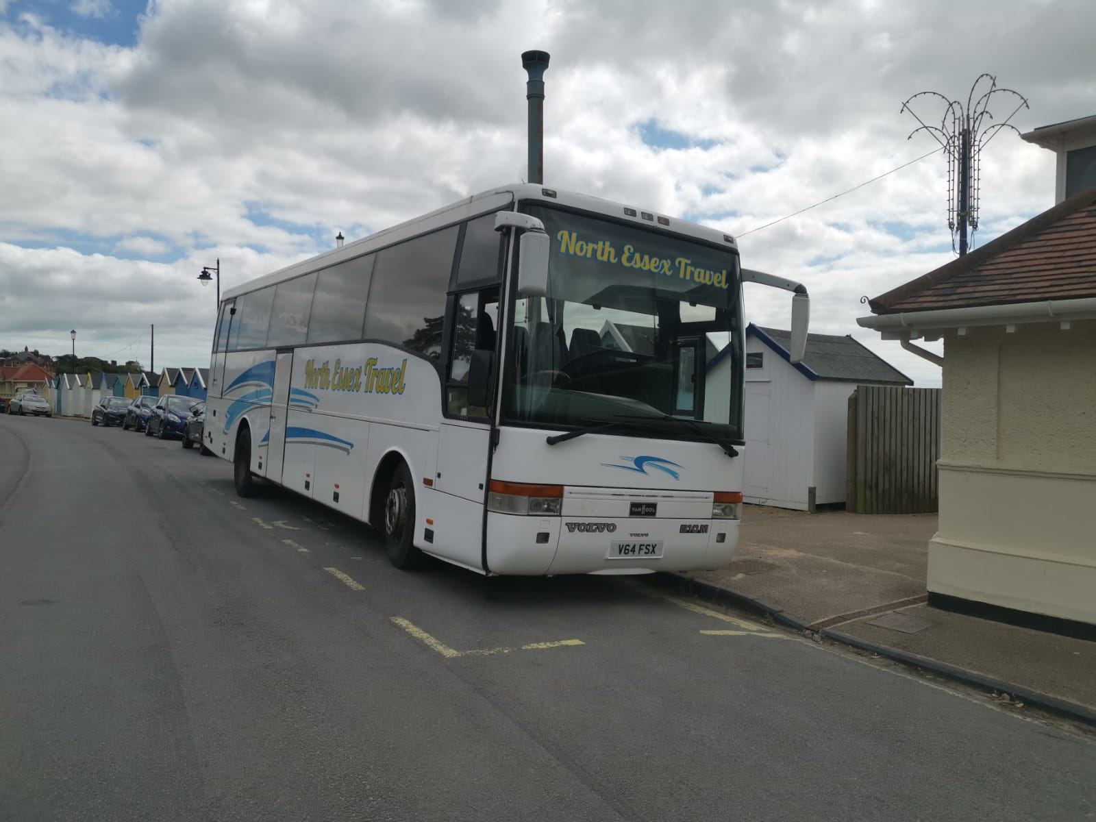 White North Essex Travel coach parked on a quiet street beside a small cream building under a cloudy sky